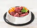 Un cuenco de metal lleno de trozos de carne cruda y zanahoria rallada, perfecto para una dieta BARF perros casera.