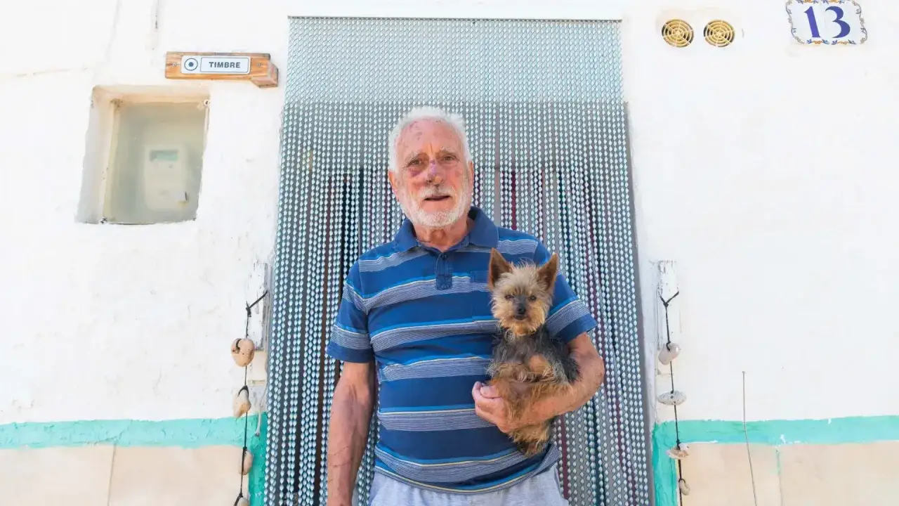 Un hombre mayor con un perro yorkshire en brazos, frente a una cortina de cuentas. Mi perro no ladra, pero me acompaña siempre.